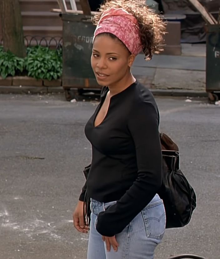 a woman with a pink bandana on her head walking down the street while holding a black bag