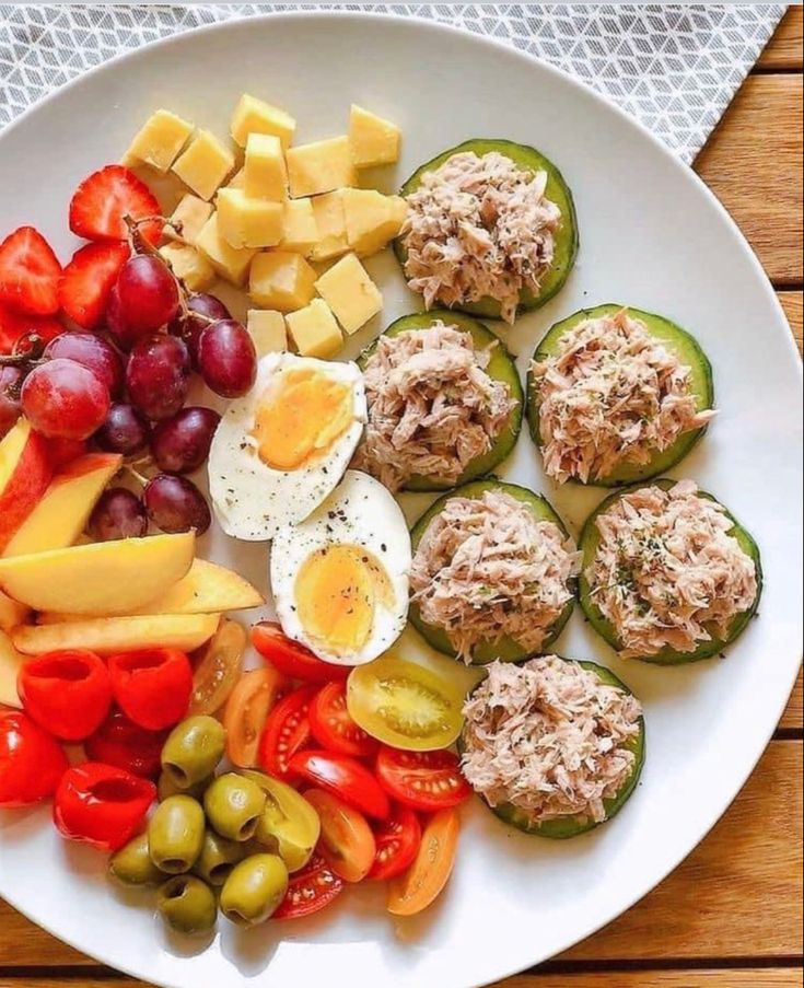 a white plate topped with cucumbers, tomatoes, cheese and other food items