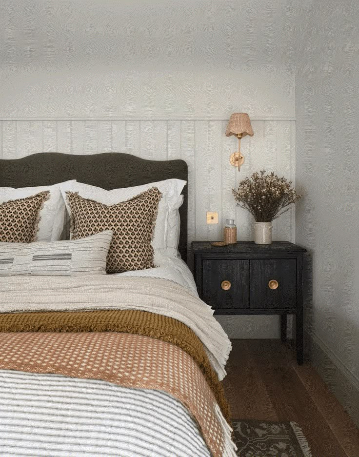 a bed with white and brown pillows in a bedroom next to a night stand filled with flowers