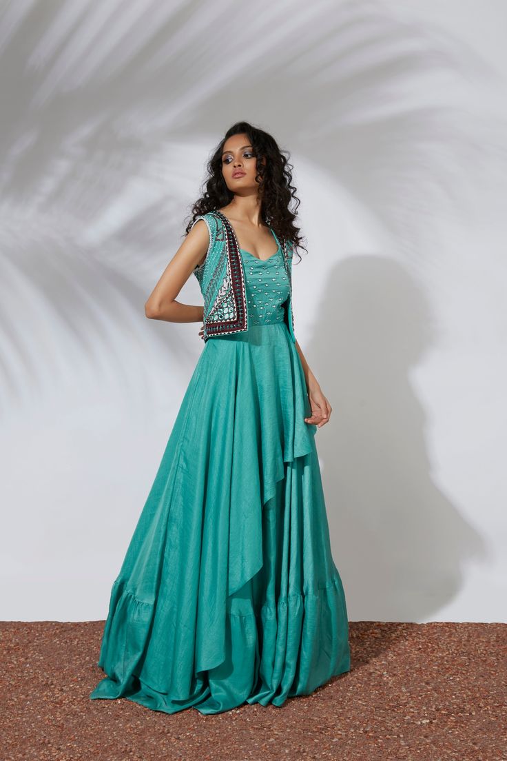 Aqua layered anarkali gown paired with a cropjacket embroidered with thread, tubes, pearls, beads & mirrors. Indulge in the captivating allure of Aqua Gown. This layered anarkali gown is thoughtfully paired with a delicate cropjacket adorned with exquisite thread, tubes, pearls, beads, and mirrors. Elevate your style with this statement piece that exudes elegance and sophistication. Colour : AQUA Fabric : CREPE Embroidery details : HAND EMBROIDERY Components : 2 Wash Care : DRY CLEAN ONLY Delive Anarkali Style Hand Embellished Maxi Lehenga, Hand Embellished Maxi Gown For Designer Wear, Designer Hand Embellished Maxi Gown, Designer Wear Hand Embellished Maxi Gown, Designer Hand-embellished Maxi Gown, Embellished Floor-length Chinon Dress, Embellished Chinon Floor-length Dress, Bollywood Style Hand Embellished Maxi Lehenga, Festive Hand Embellished Maxi Lehenga