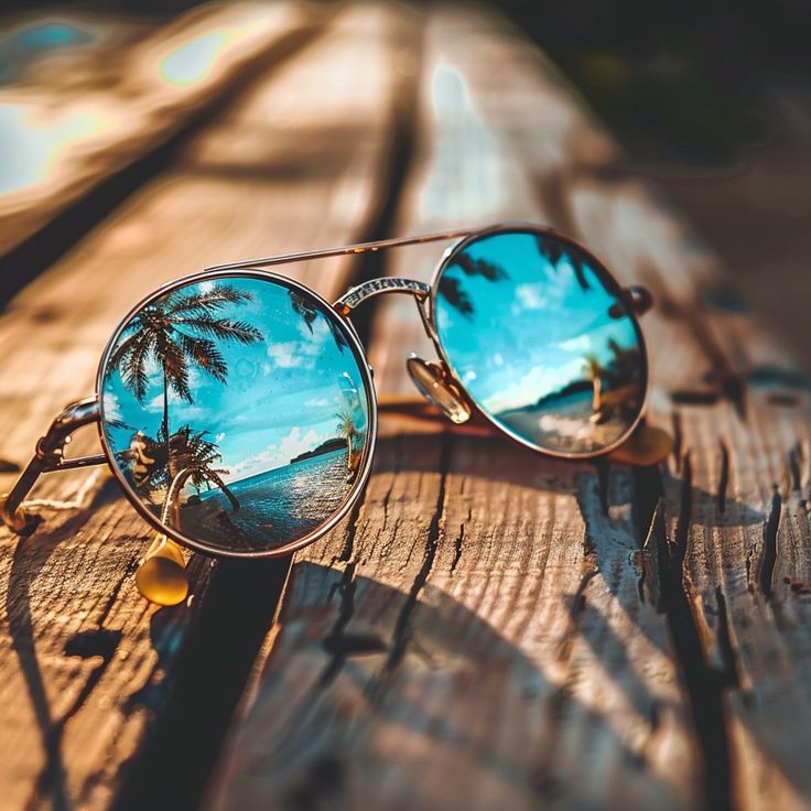 a pair of sunglasses sitting on top of a wooden table with palm trees reflected in them