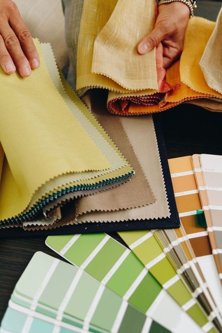 a person is holding some fabric in front of color swatches and paint samples on the table