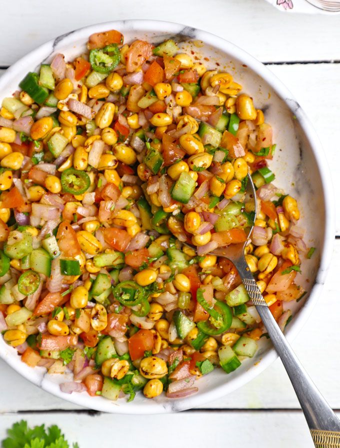 a bowl filled with corn and vegetables on top of a white table next to a spoon