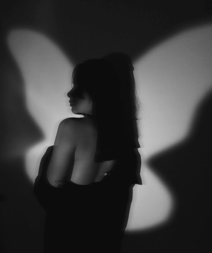 a woman standing in front of a wall with the shadow of a butterfly on it