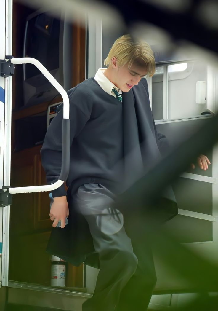 a young man wearing a sweater and tie is walking down the stairs with his hands in his pockets