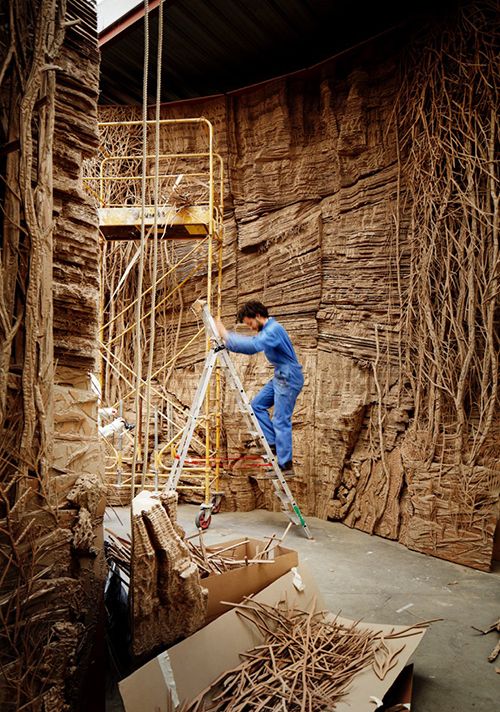 a man on a ladder in front of a wall with vines growing up it's sides