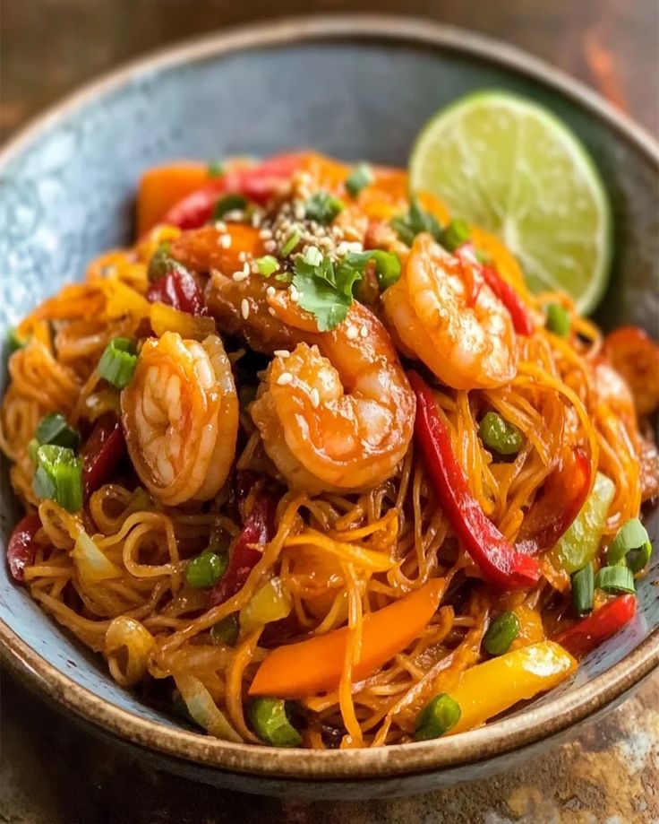 a close up of a plate of food with shrimp and vegetables on it, next to a lime wedge