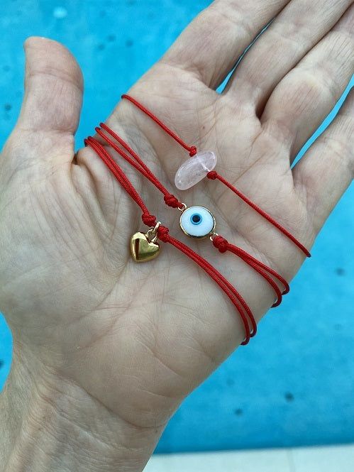 a hand holding three bracelets with evil eye charms on them and a heart charm