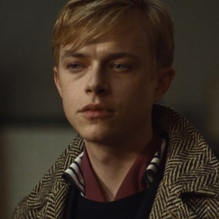 a young man with blonde hair wearing a coat