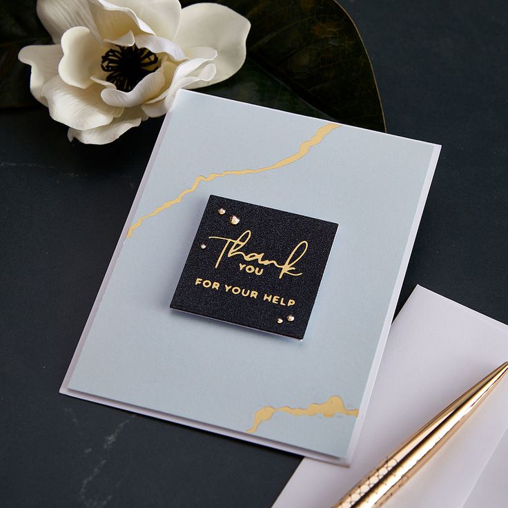 a thank you card with gold foil on it next to a white flower and pen