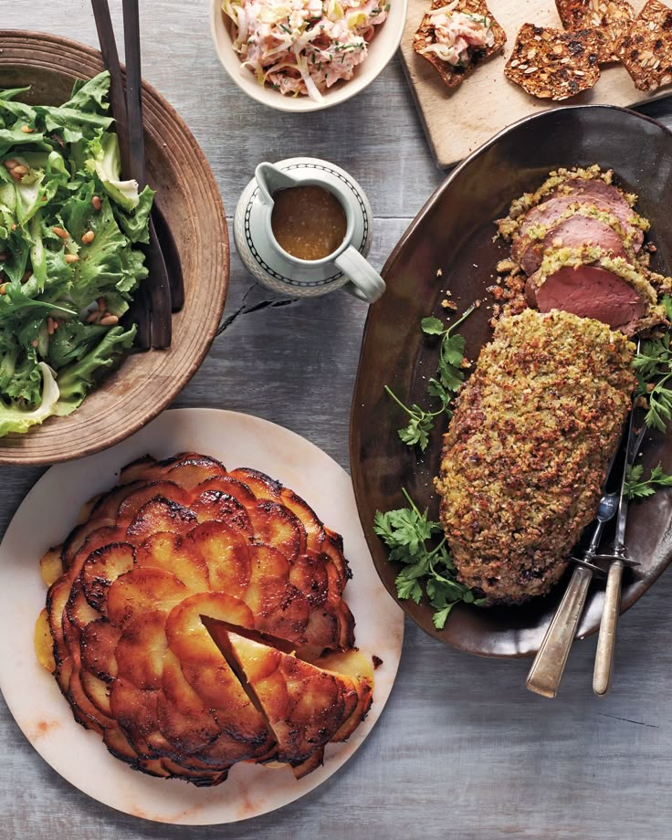 a table topped with plates and bowls filled with food next to pies and salad