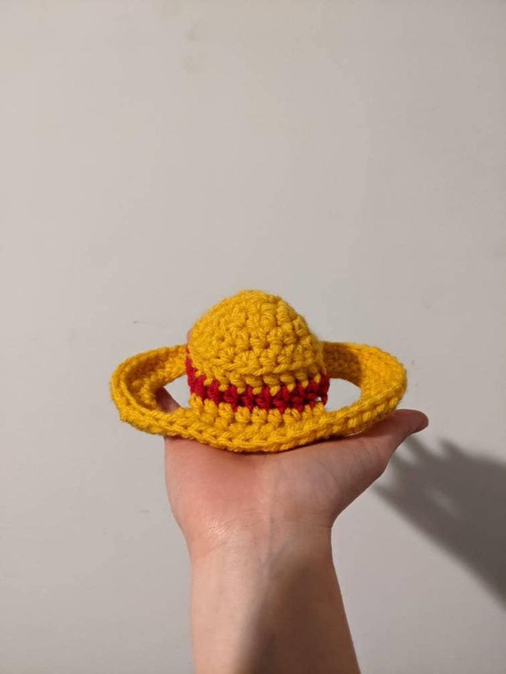 a hand holding a small yellow crocheted hat with a red stripe around the brim