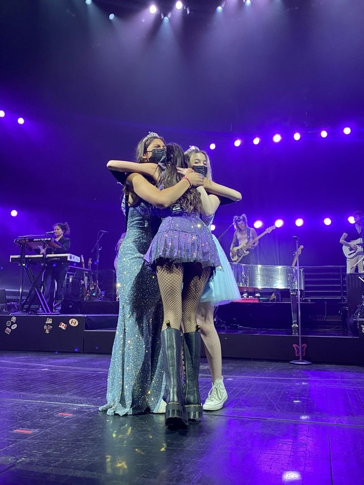 three women hugging each other on stage in front of purple lights and blue lighting behind them