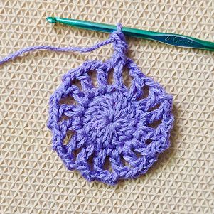 a crocheted doily with a green knitting needle next to it on a piece of fabric