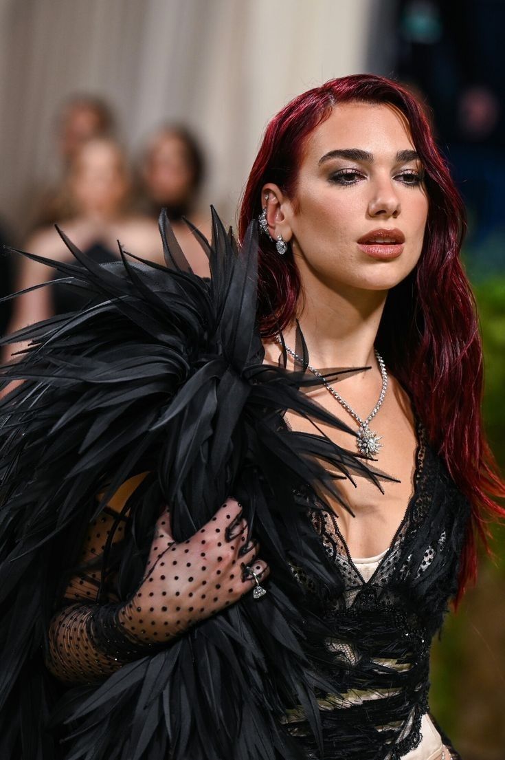 a woman with red hair wearing a black feathered dress and gloves on the runway