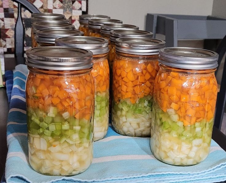 several mason jars filled with chopped vegetables sitting on a blue and white striped towel next to a table