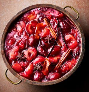 a pot filled with cranberry sauce on top of a wooden table next to cinnamon sticks