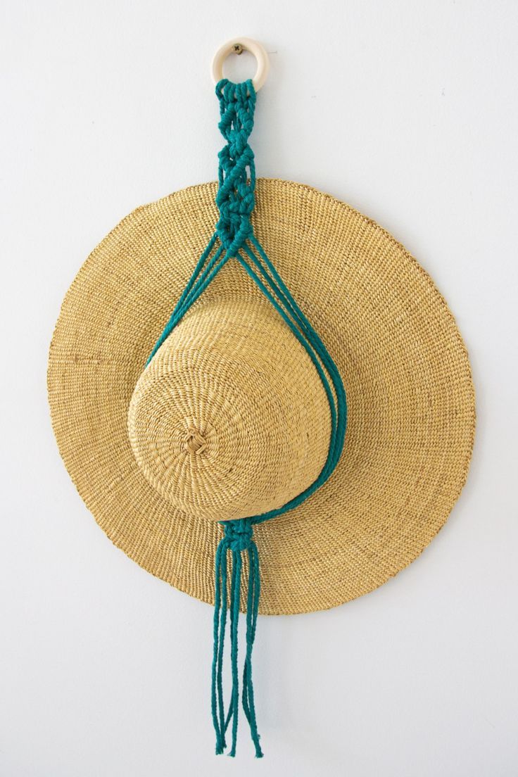 a straw hat hanging on the wall next to a green tasseled string and a white hook