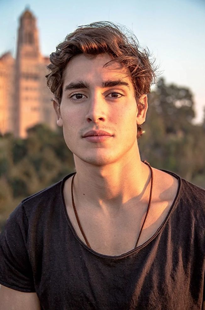 a young man in a black shirt is posing for the camera with a cityscape behind him