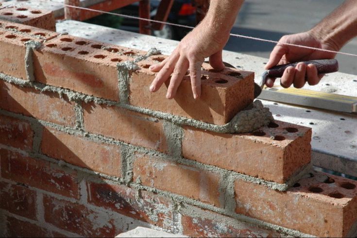 a brick wall being constructed with bricks and cements, while two hands are on top of it