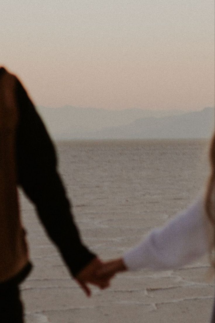 two people holding hands while walking on the beach