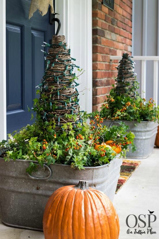 two pumpkins sitting on the front porch next to some plants and trees in buckets