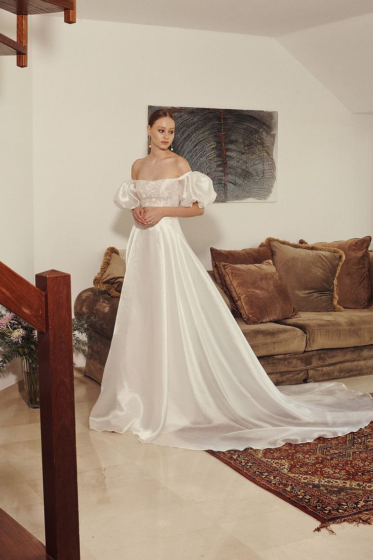 a woman in a white wedding dress standing next to a brown couch and coffee table