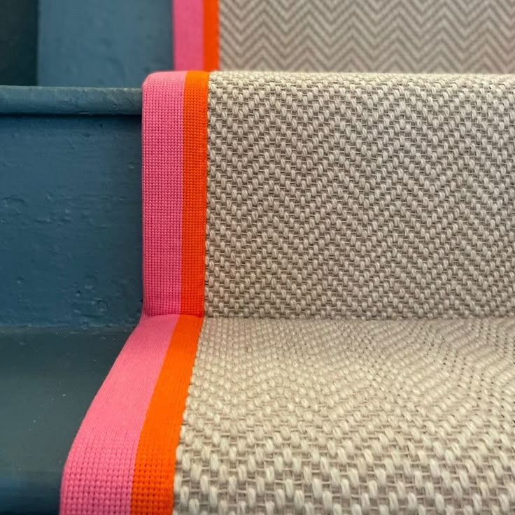 an orange and pink striped rug sitting on top of a blue stair case next to a wall