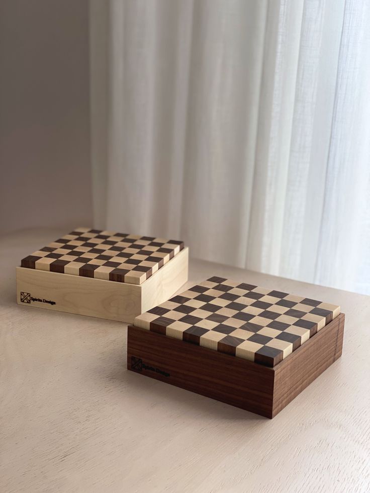 two wooden boxes sitting on top of a white table next to each other with black and white checkered designs