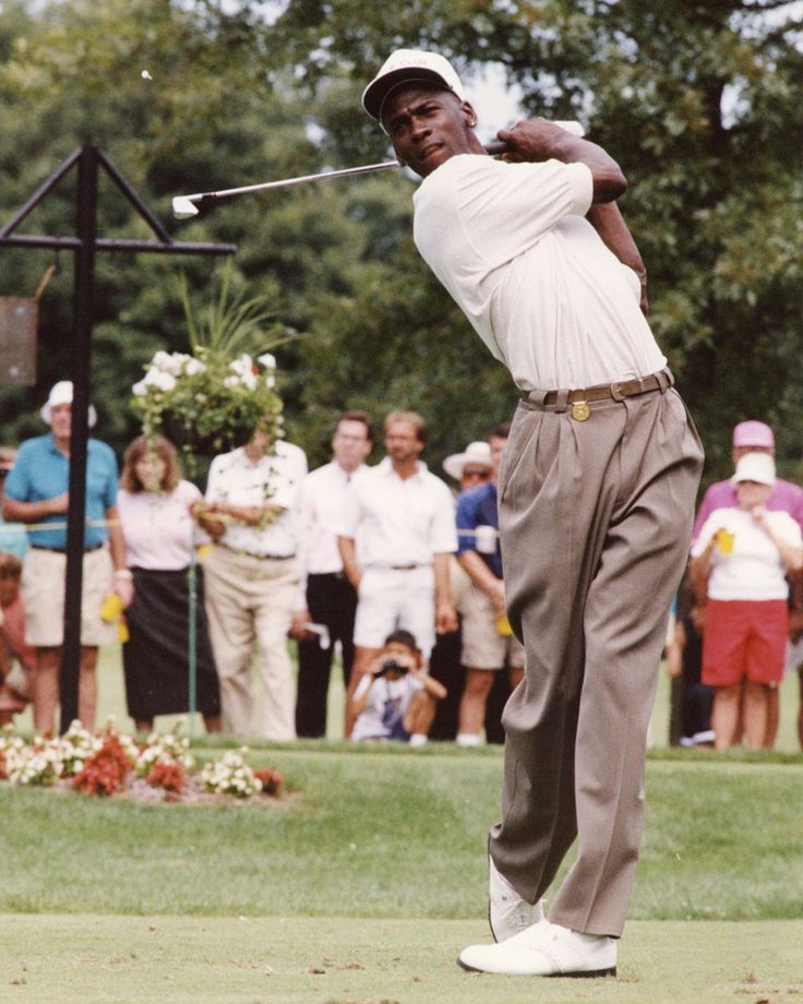 a man swinging a golf club on top of a lush green field with people watching