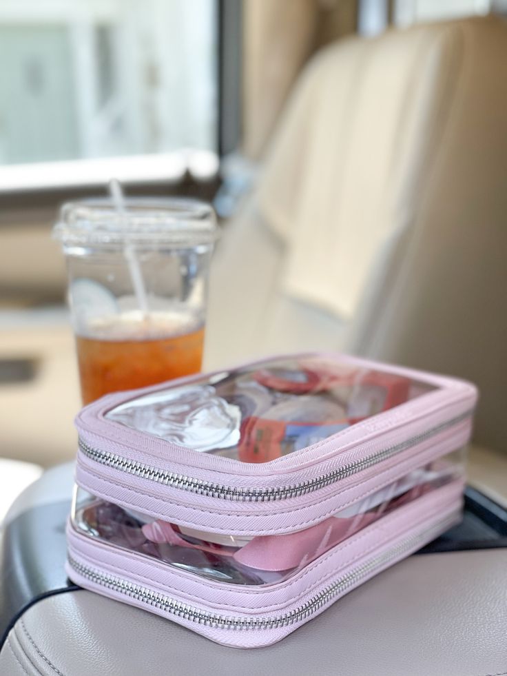 two zippered bags sitting on top of a seat next to a drink in a cup