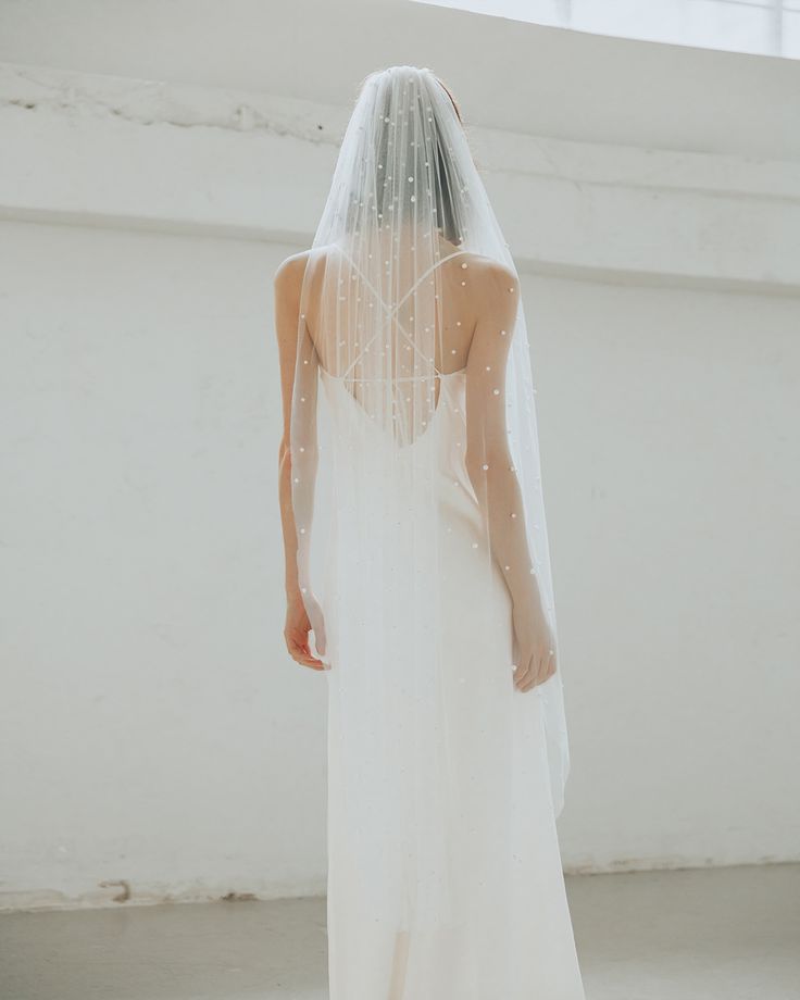 a woman in a white wedding dress with a veil on her head is looking down at the floor