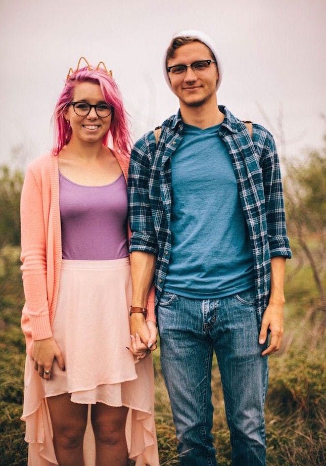 a man and woman standing next to each other in front of some trees with pink hair