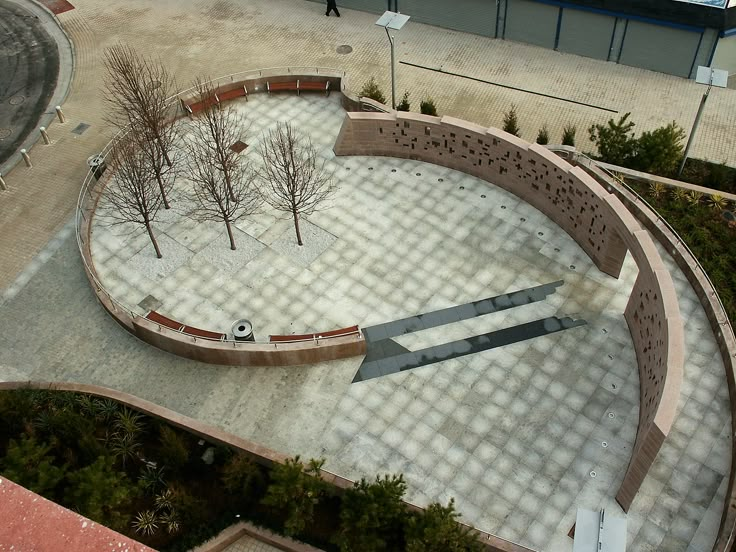 an aerial view of a circular courtyard with benches and trees in the center, surrounded by concrete blocks