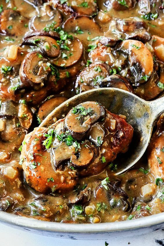 a spoon full of mushrooms and meat in a white dish with parsley on top