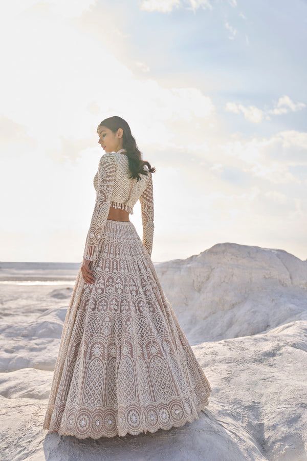 a woman standing on top of a snow covered hill wearing a long white skirt and jacket