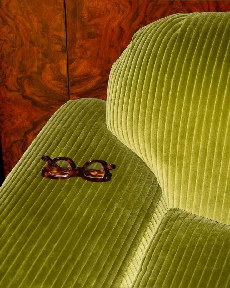 a pair of glasses sitting on top of a green velvet chair with wood trimmings