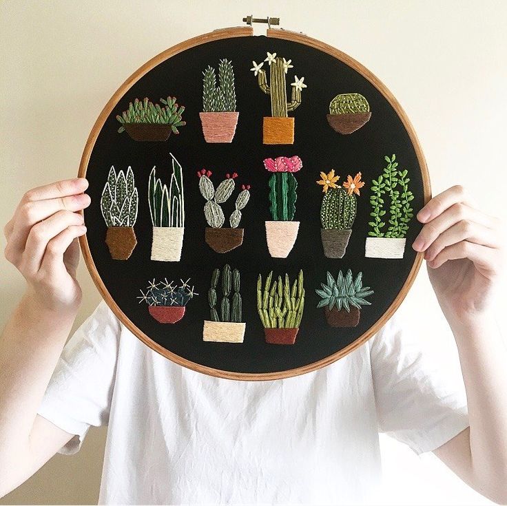 a woman is holding up a black embroidery art piece with potted plants on it