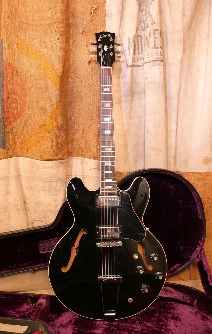 an electric guitar sitting on top of a purple velvet case in front of a curtain