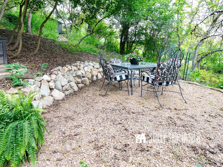 a table and chairs sitting on top of a dirt field next to a tree filled hillside