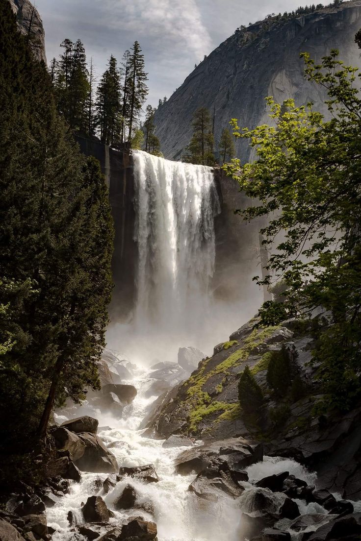 a waterfall with water flowing down it surrounded by rocks and trees in the foreground