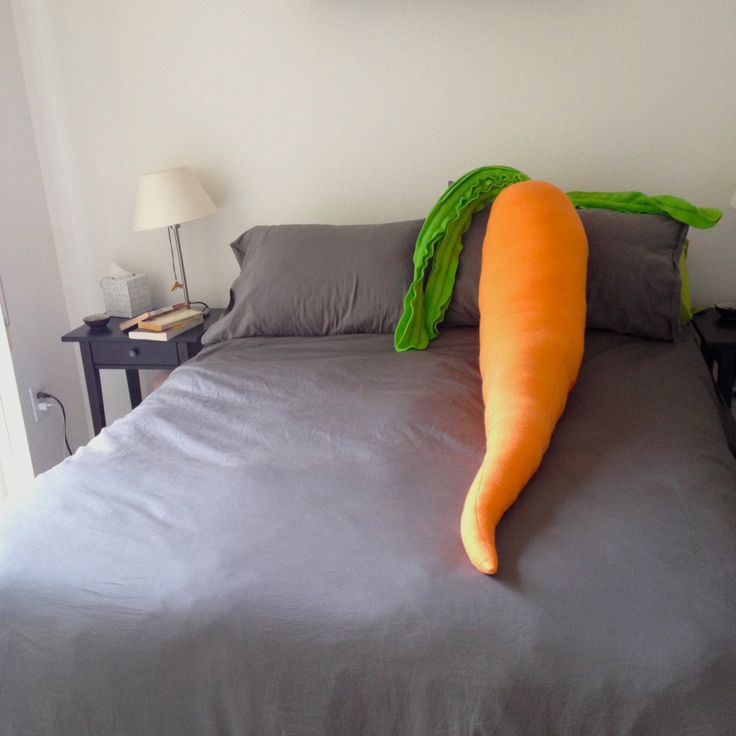 a large carrot laying on top of a bed next to a night stand and lamp