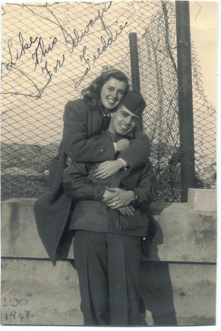 black and white photograph of two people hugging each other in front of a chain link fence