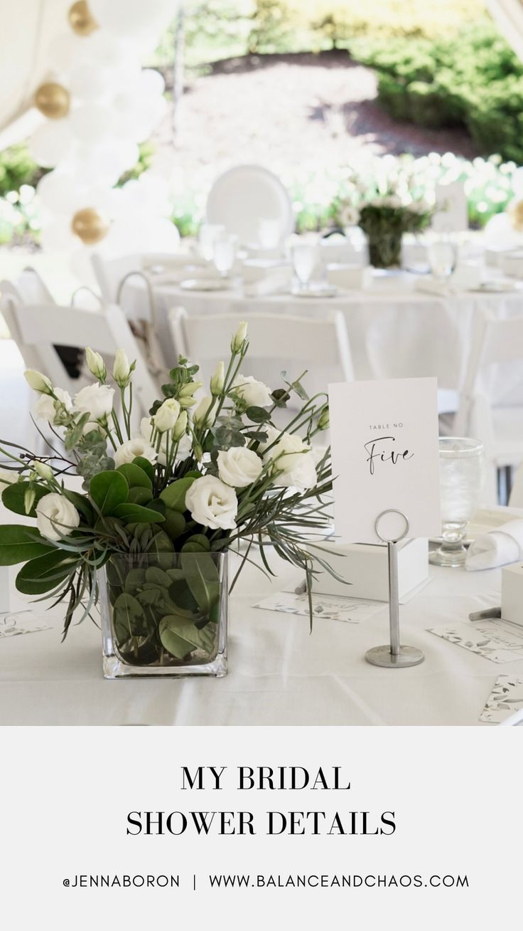 a table with white flowers and greenery in a clear vase on top of it