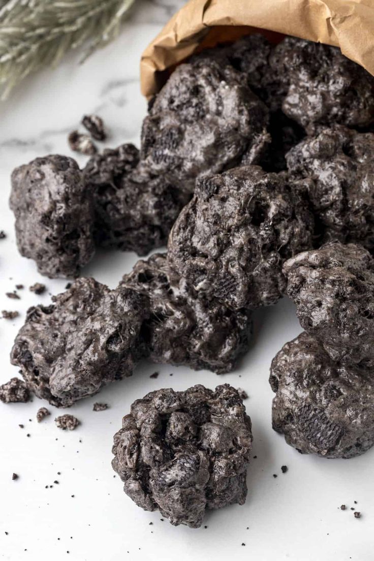 chocolate cookies are sitting on a white surface next to a brown paper bag and sprig of rosemary