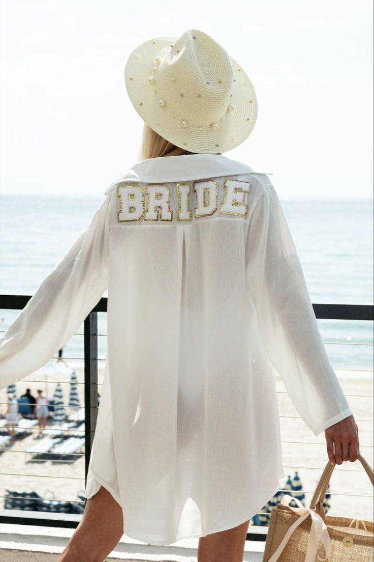 a woman in a white shirt and hat is walking by the beach with her hand on her hip