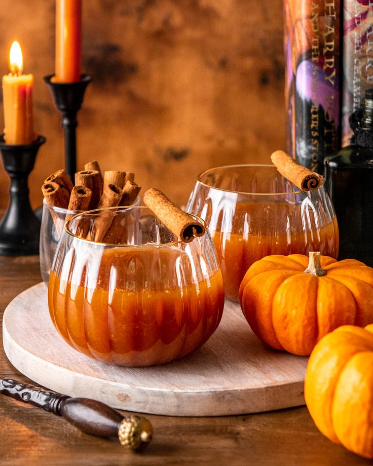 two glasses filled with liquid sitting on top of a table next to some pumpkins