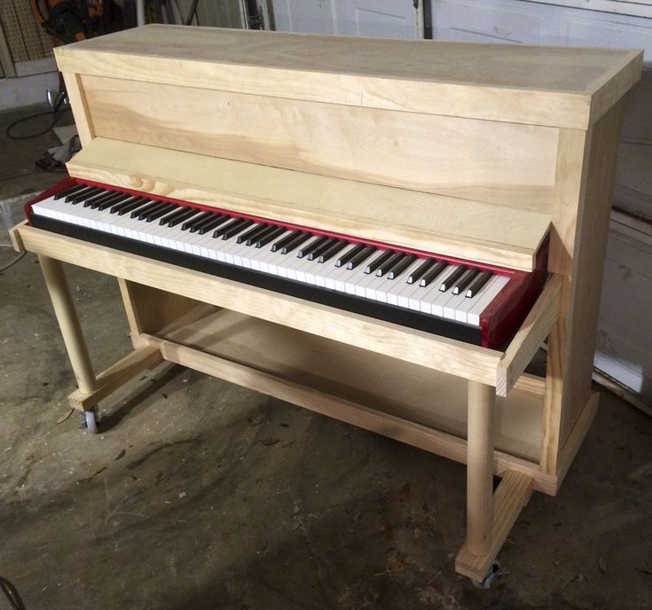 a wooden piano sitting on top of a table in a garage next to a wall