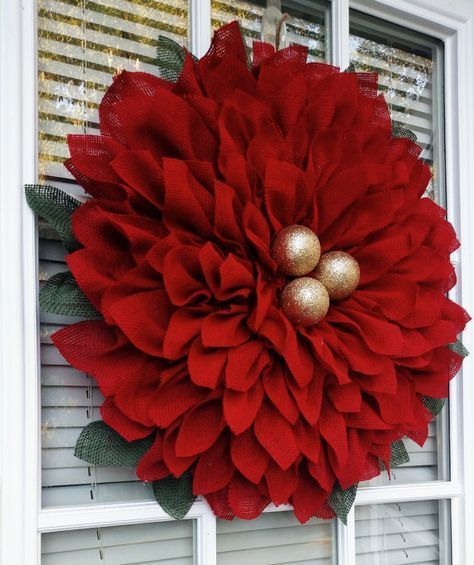 a large red flower hanging on the side of a window with gold balls in it