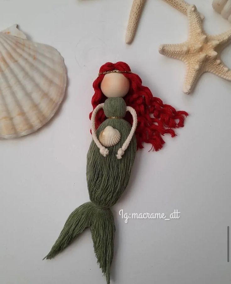 a mermaid doll with red hair laying on top of a table next to shells and starfish